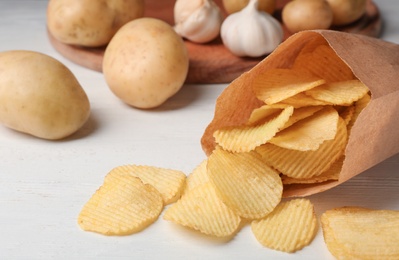 Paper bag of crispy potato chips on white wooden table. Space for text