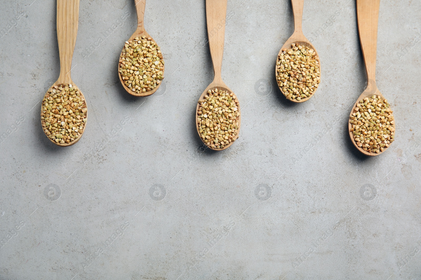 Photo of Uncooked green buckwheat grains in spoons on light table, flat lay. Space for text