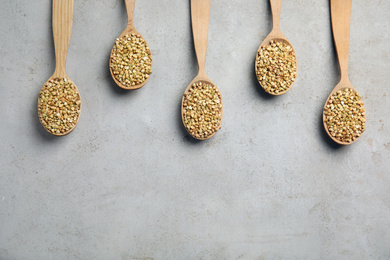 Photo of Uncooked green buckwheat grains in spoons on light table, flat lay. Space for text