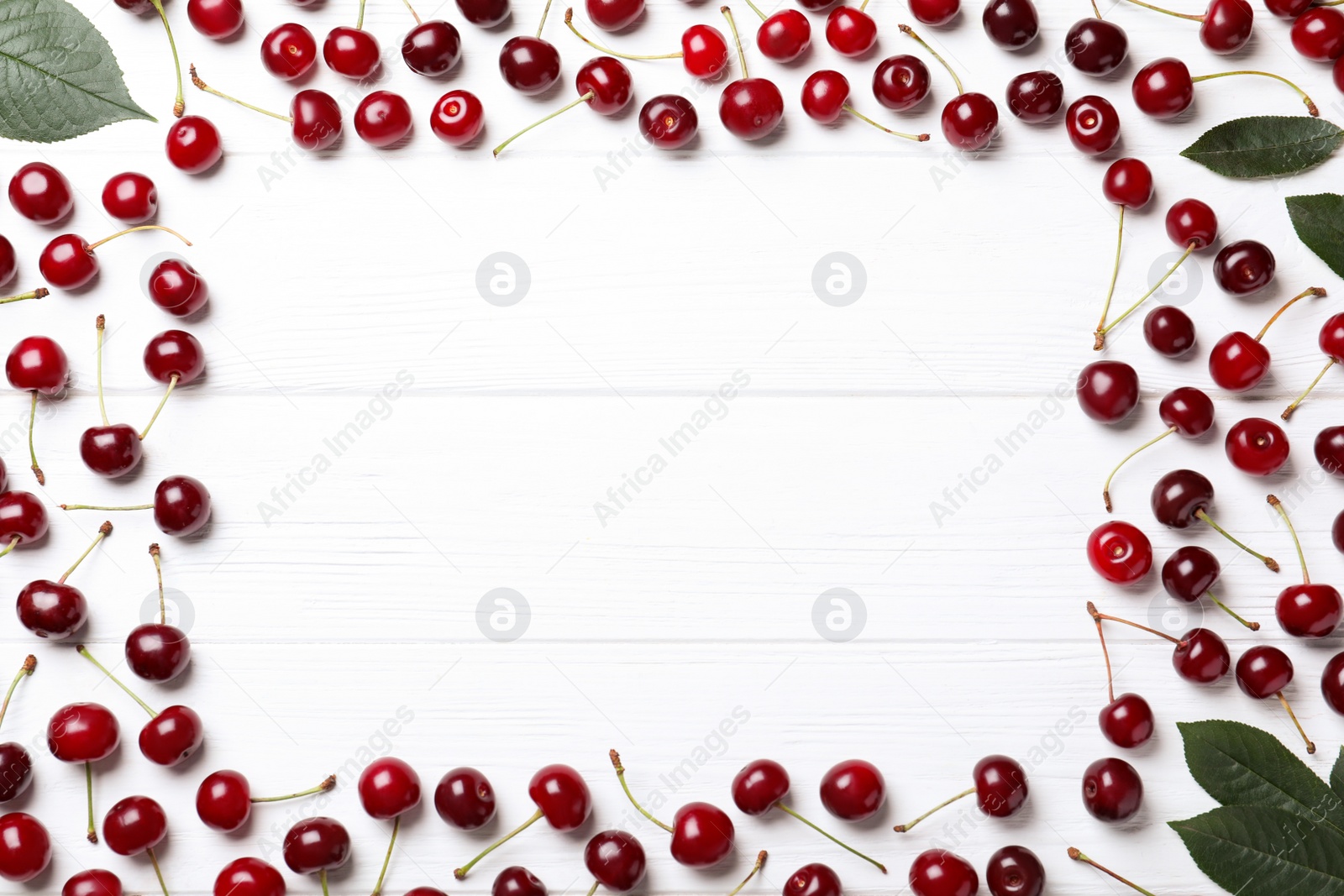 Photo of Frame of sweet juicy cherries and leaves on white wooden table, flat lay. Space for text