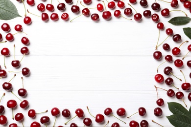 Frame of sweet juicy cherries and leaves on white wooden table, flat lay. Space for text