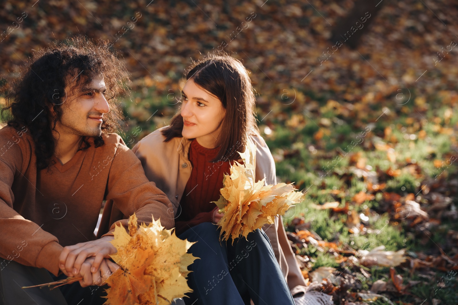 Photo of Happy young couple with dry leaves spending time together in autumn park, space for text. Dating agency