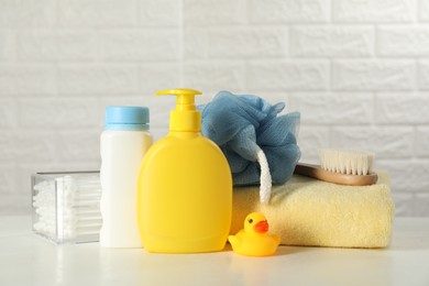 Photo of Baby cosmetic products, bath duck, brush and towel on white table against brick wall