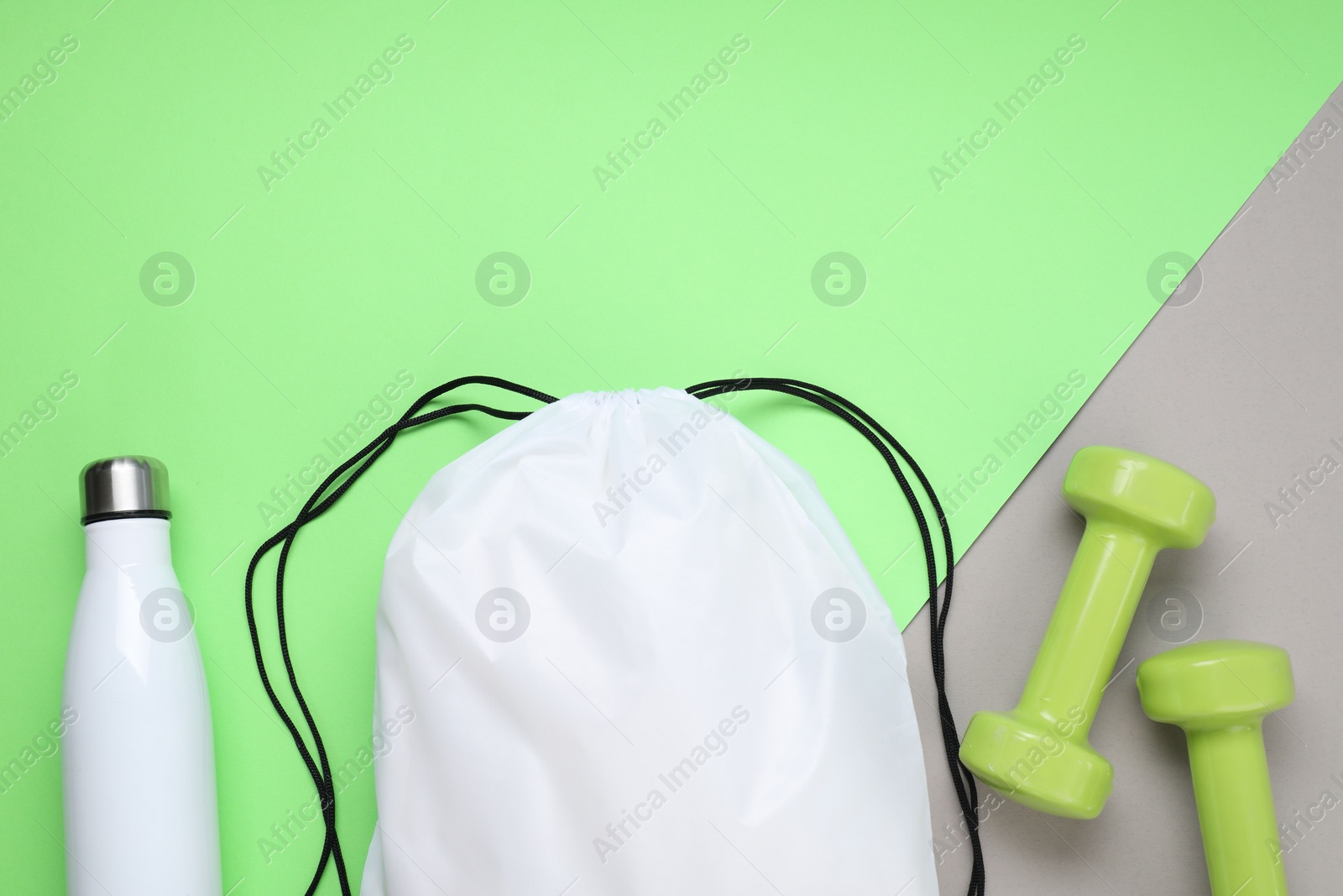 Photo of White drawstring bag, thermo bottle and dumbbells on color background, flat lay. Space for text