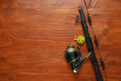 Fishing rod with reel and bait on wooden table, flat lay. Space for text