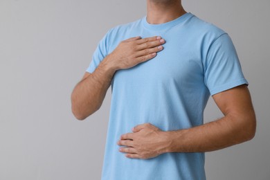 Photo of Man holding hands near chest on grey background, closeup. Space for text