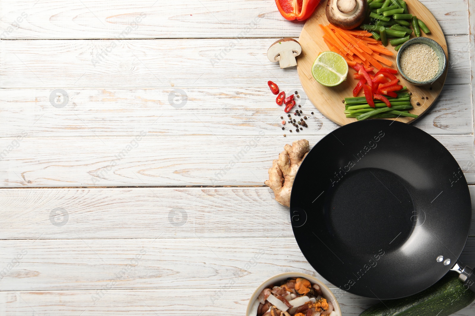 Photo of Flat lay composition with black wok and products on light wooden table. Space for text