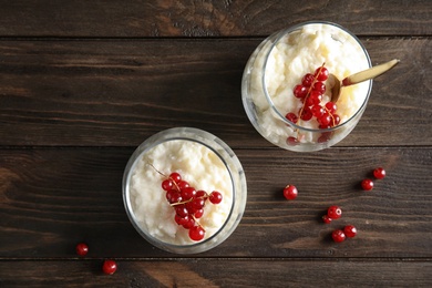 Photo of Creamy rice pudding with red currant in glasses and berries on wooden background, top view. Space for text