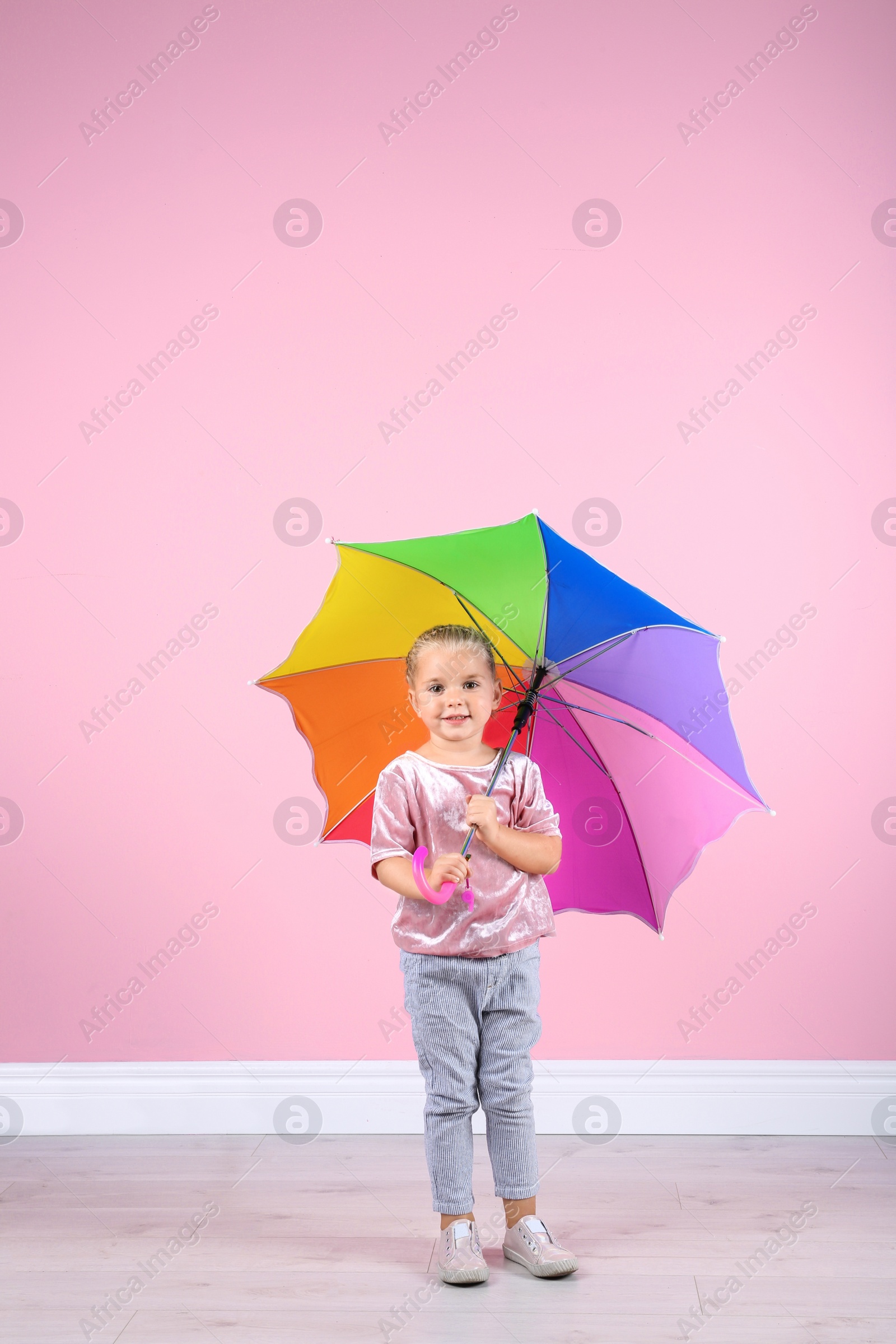 Photo of Little girl with rainbow umbrella near color wall. Space for text