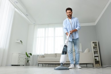 Photo of Happy man cleaning floor with steam mop at home, low angle view