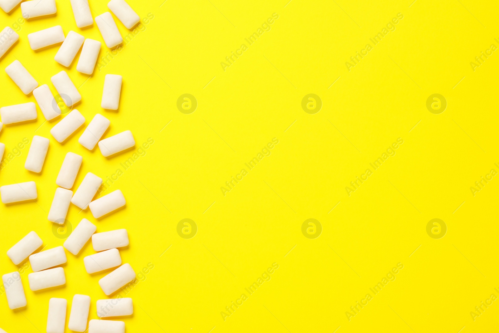 Photo of Many chewing gum pieces on yellow background, flat lay. Space for text