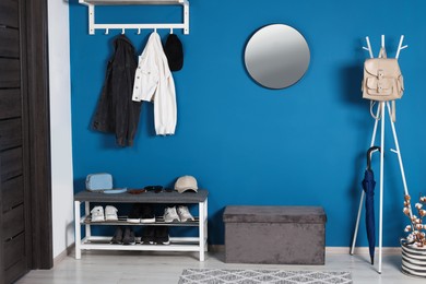 Photo of Stylish hallway with coat rack and shoe storage bench near blue wall. Interior design