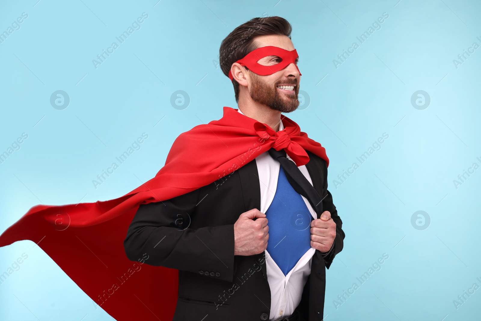 Photo of Happy businessman wearing superhero costume under suit on light blue background