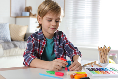 Photo of Little boy playing with plasticine at table indoors. Creative hobby