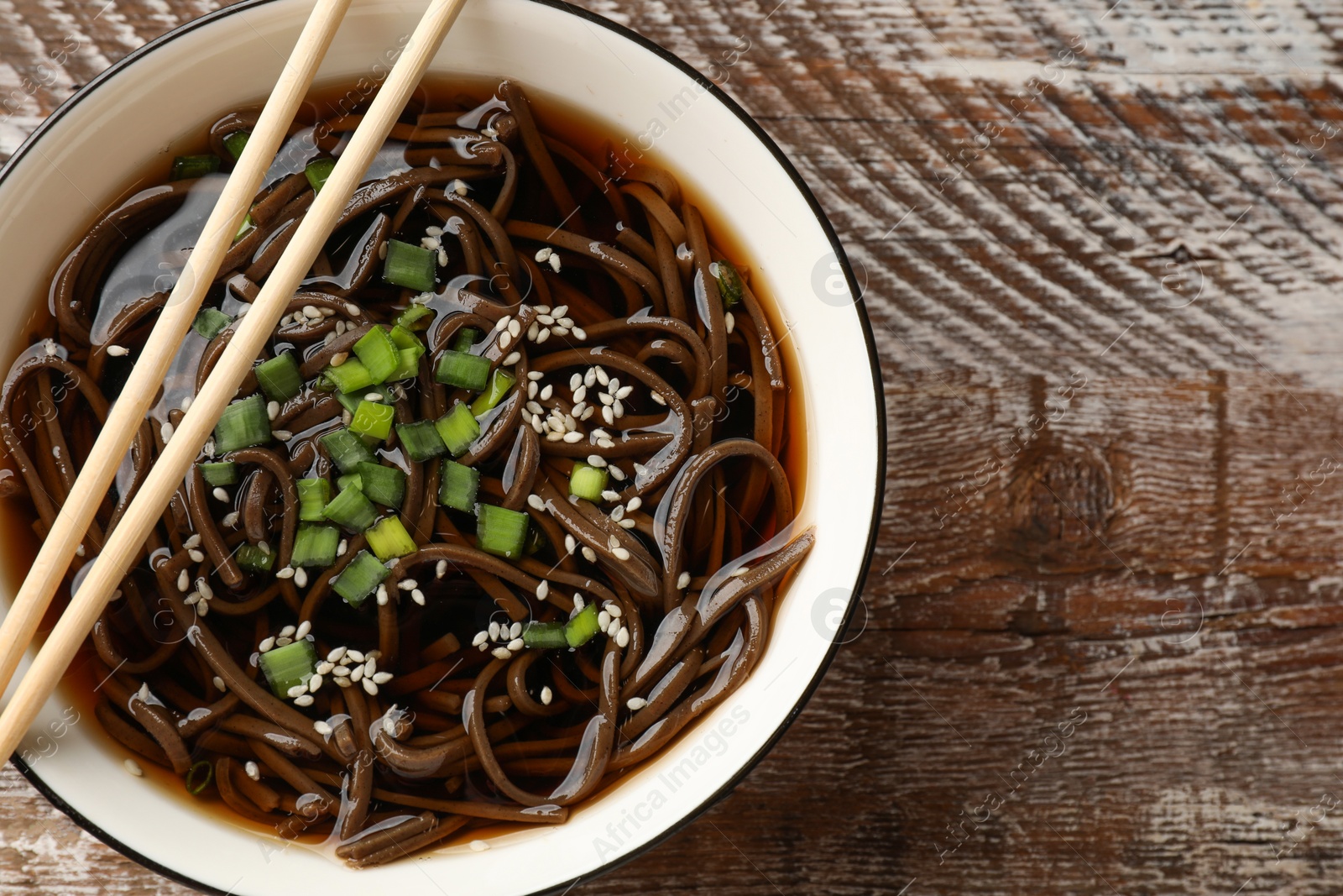 Photo of Tasty soup with buckwheat noodles (soba), onion in bowl and chopsticks on wooden table, top view. Space for text