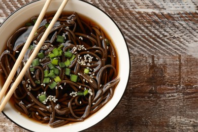 Photo of Tasty soup with buckwheat noodles (soba), onion in bowl and chopsticks on wooden table, top view. Space for text