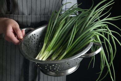 Photo of Woman holding colander with green spring onions on black background, closeup