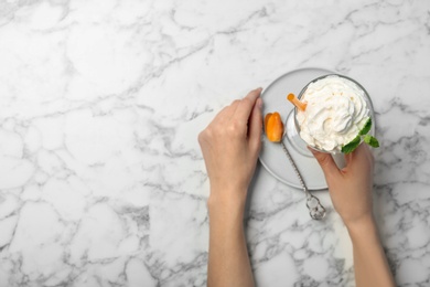 Woman holding glass of delicious milk shake with whipped cream at table, top view