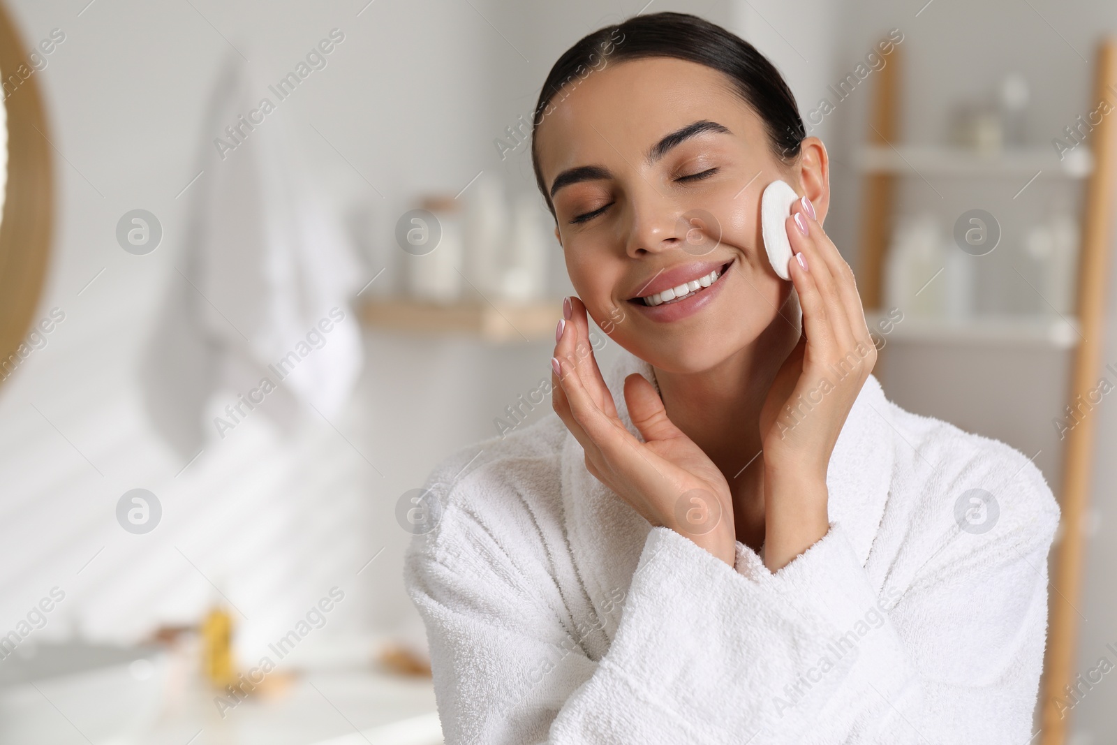 Photo of Beautiful woman removing makeup with cotton pad in bathroom, space for text