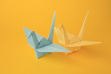 Photo of Origami art. Beautiful light blue and yellow paper cranes on orange background