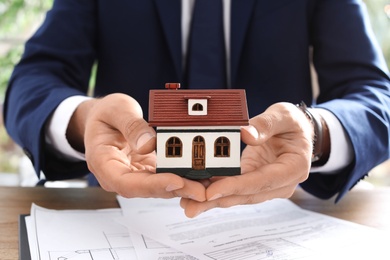 Photo of Real estate agent holding house model at table in office, closeup
