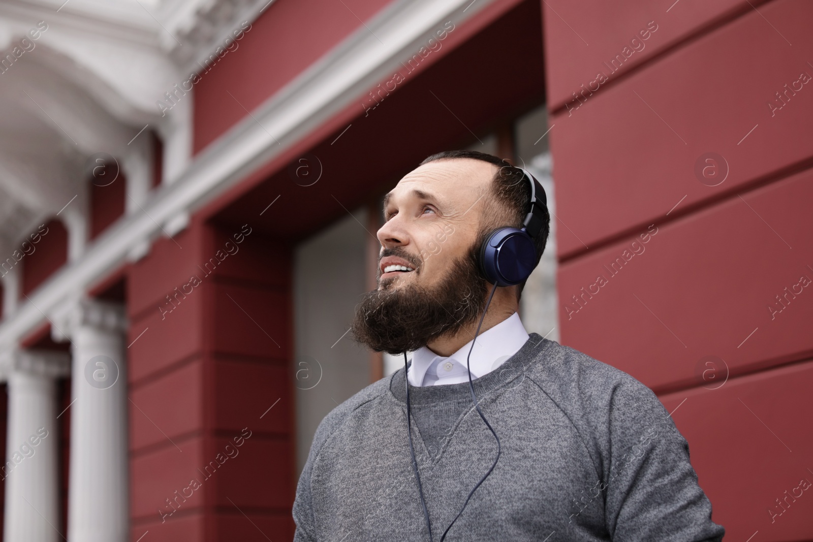 Photo of Mature man with headphones listening to music outdoors. Space for text