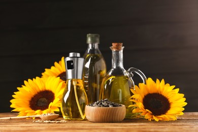 Photo of Many different bottles with cooking oil, sunflower seeds and flowers on wooden table against dark background