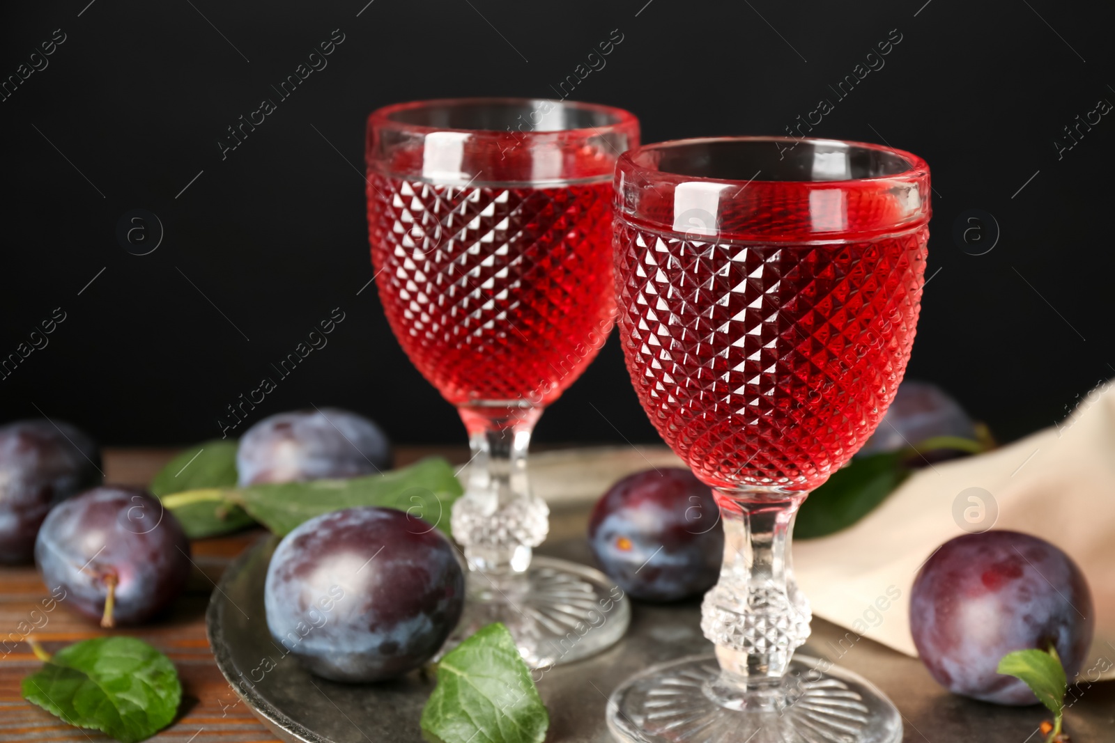 Photo of Delicious plum liquor and ripe fruits on wooden table against black background. Homemade strong alcoholic beverage
