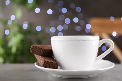 Photo of Cup of tea and wafers on grey table against blurred lights, space for text