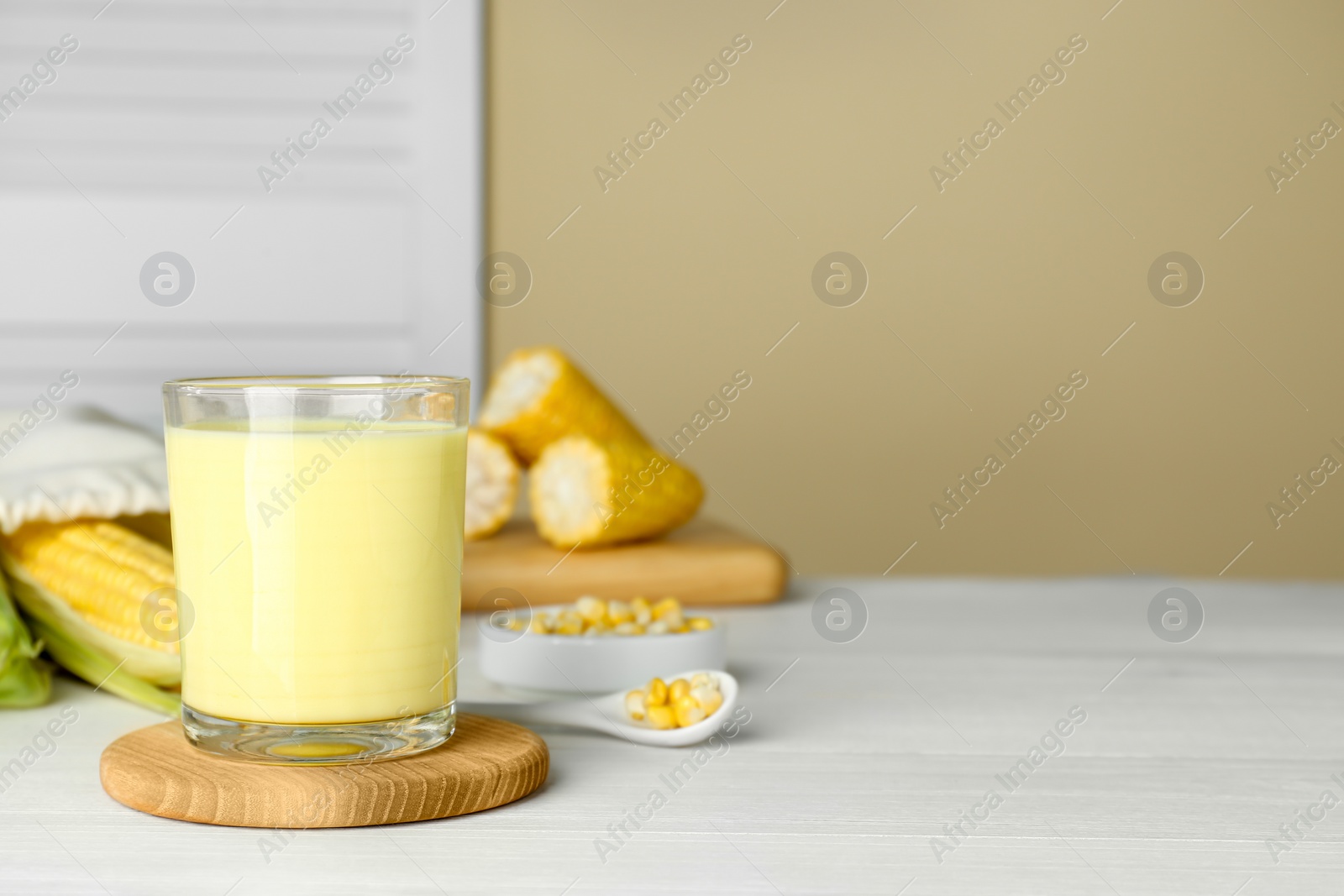 Photo of Tasty fresh corn milk in glass and cobs on white wooden table, space for text