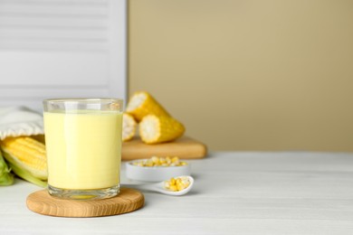 Photo of Tasty fresh corn milk in glass and cobs on white wooden table, space for text