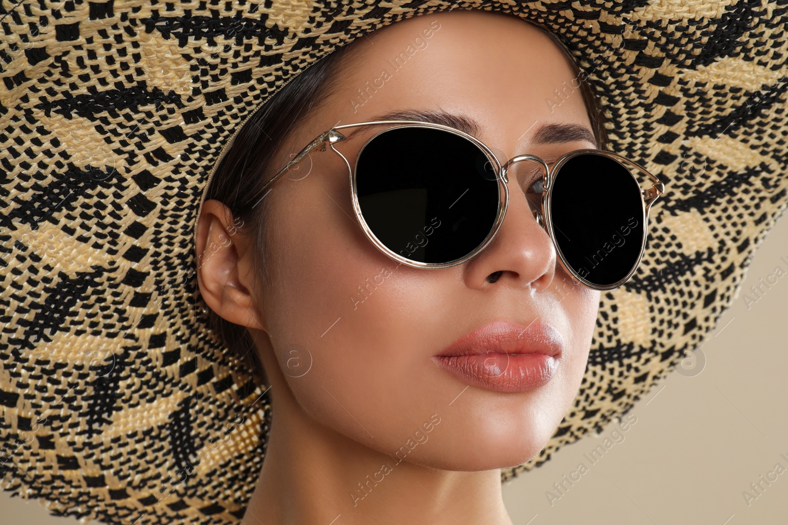 Photo of Beautiful young woman wearing sunglasses and hat on beige background, closeup