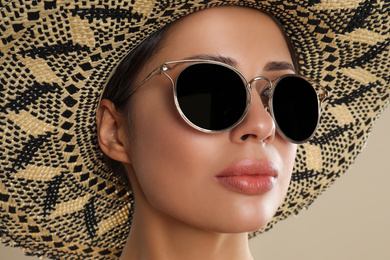 Photo of Beautiful young woman wearing sunglasses and hat on beige background, closeup