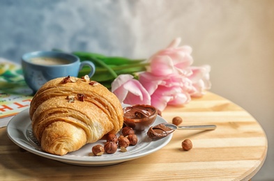 Tasty croissant with chocolate and nuts on table