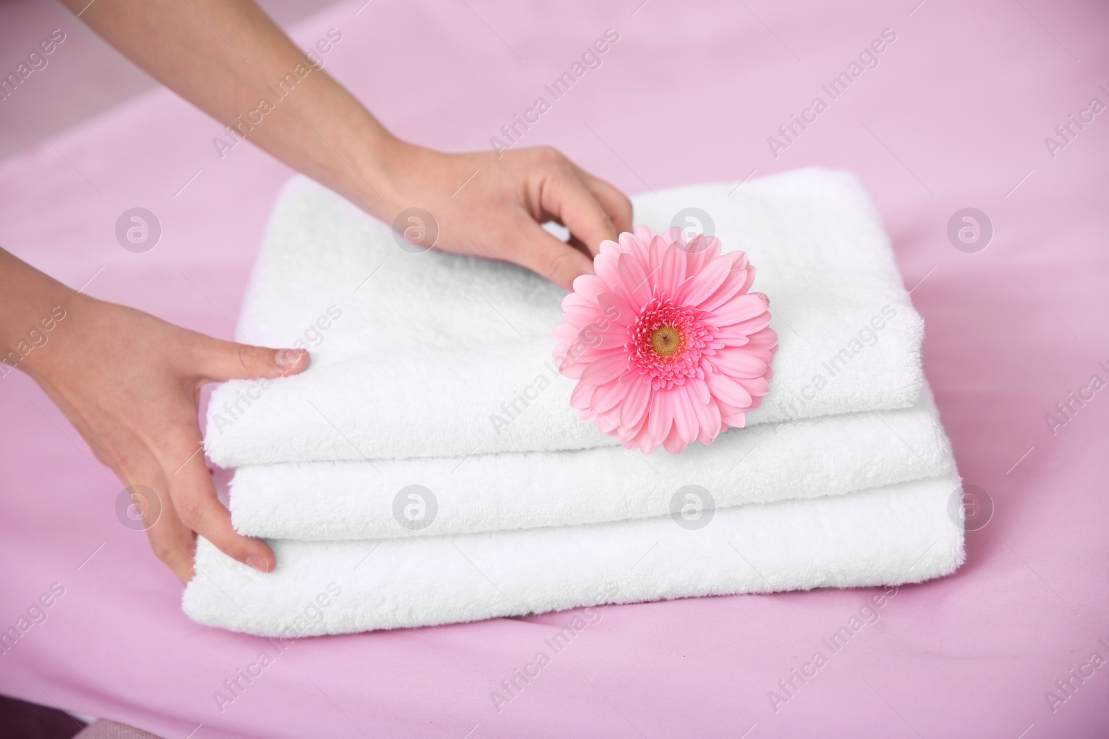 Photo of Young maid putting flower on stack of towels in hotel room