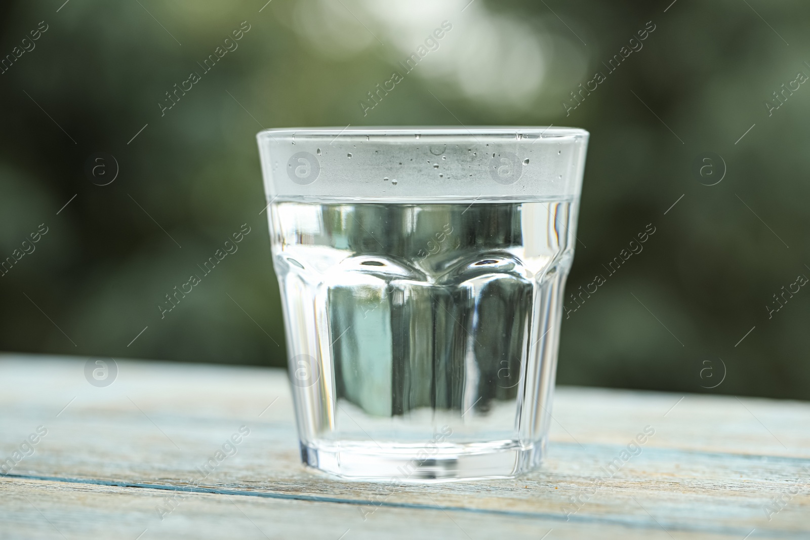 Photo of Glass of pure water on light blue wooden table against blurred background