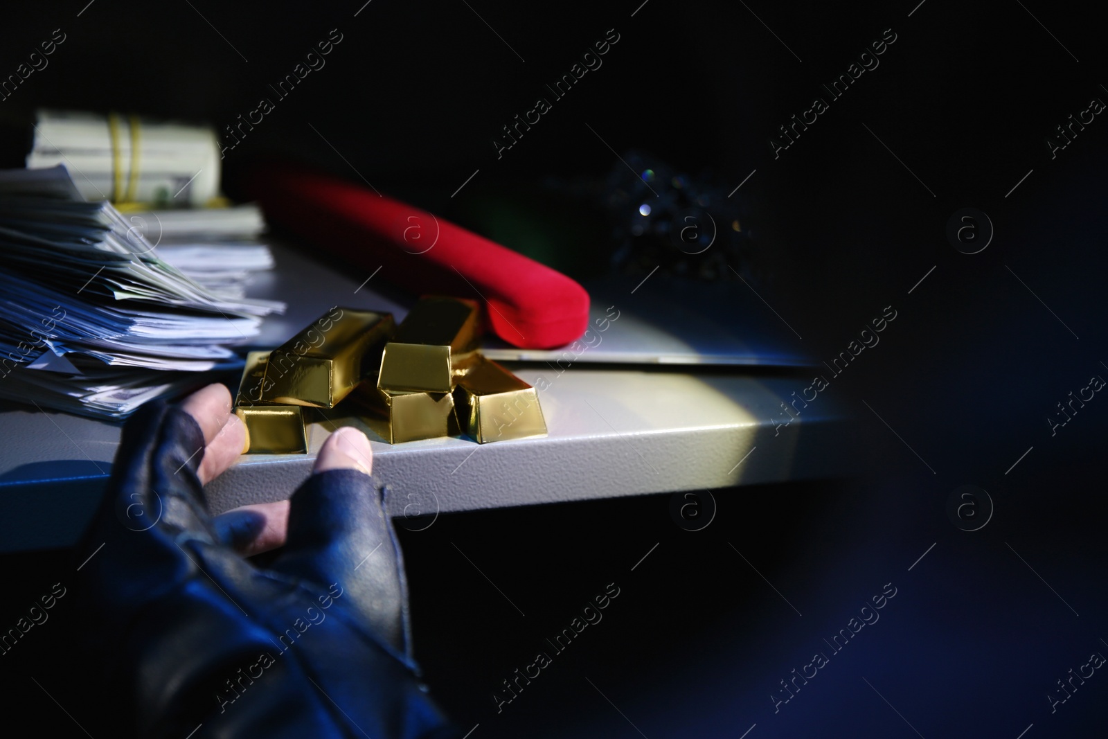 Photo of Thief taking gold bars out of steel safe indoors at night, closeup