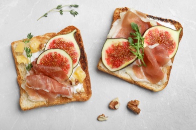 Photo of Delicious sandwiches with figs, proscuitto and cheese on light table, flat lay