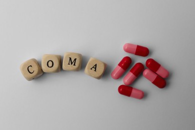 Photo of Wooden cubes with word Coma and pills on grey background, flat lay