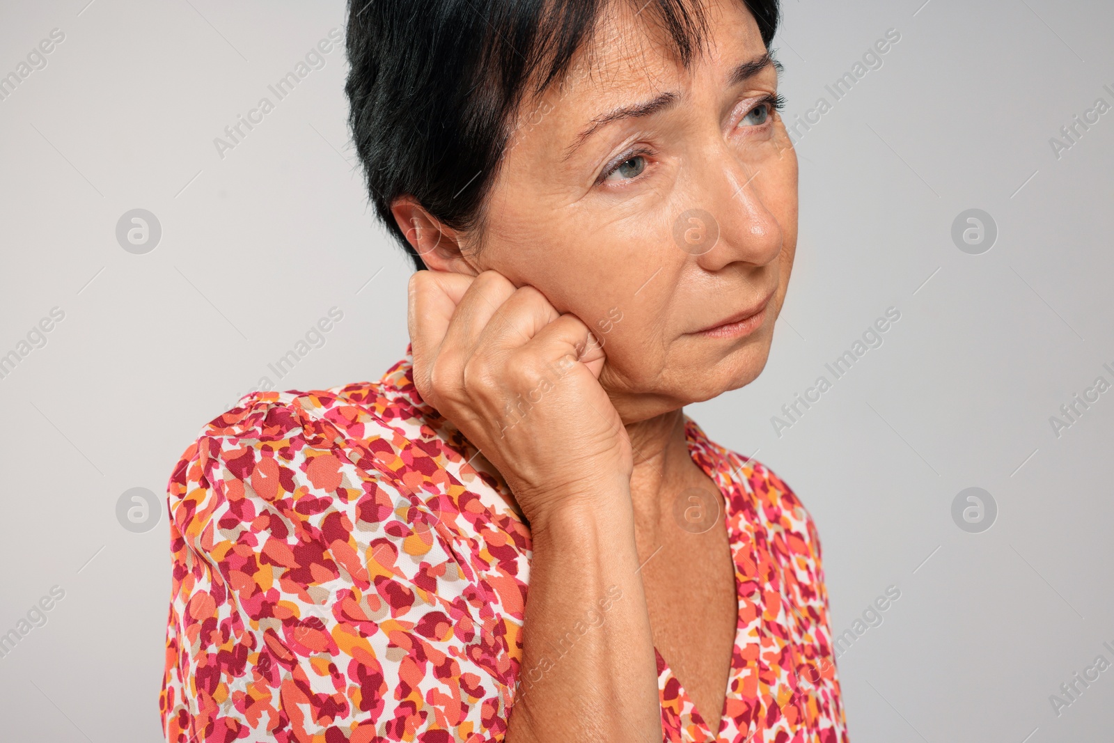 Photo of Senior woman suffering from ear pain on light grey background, closeup