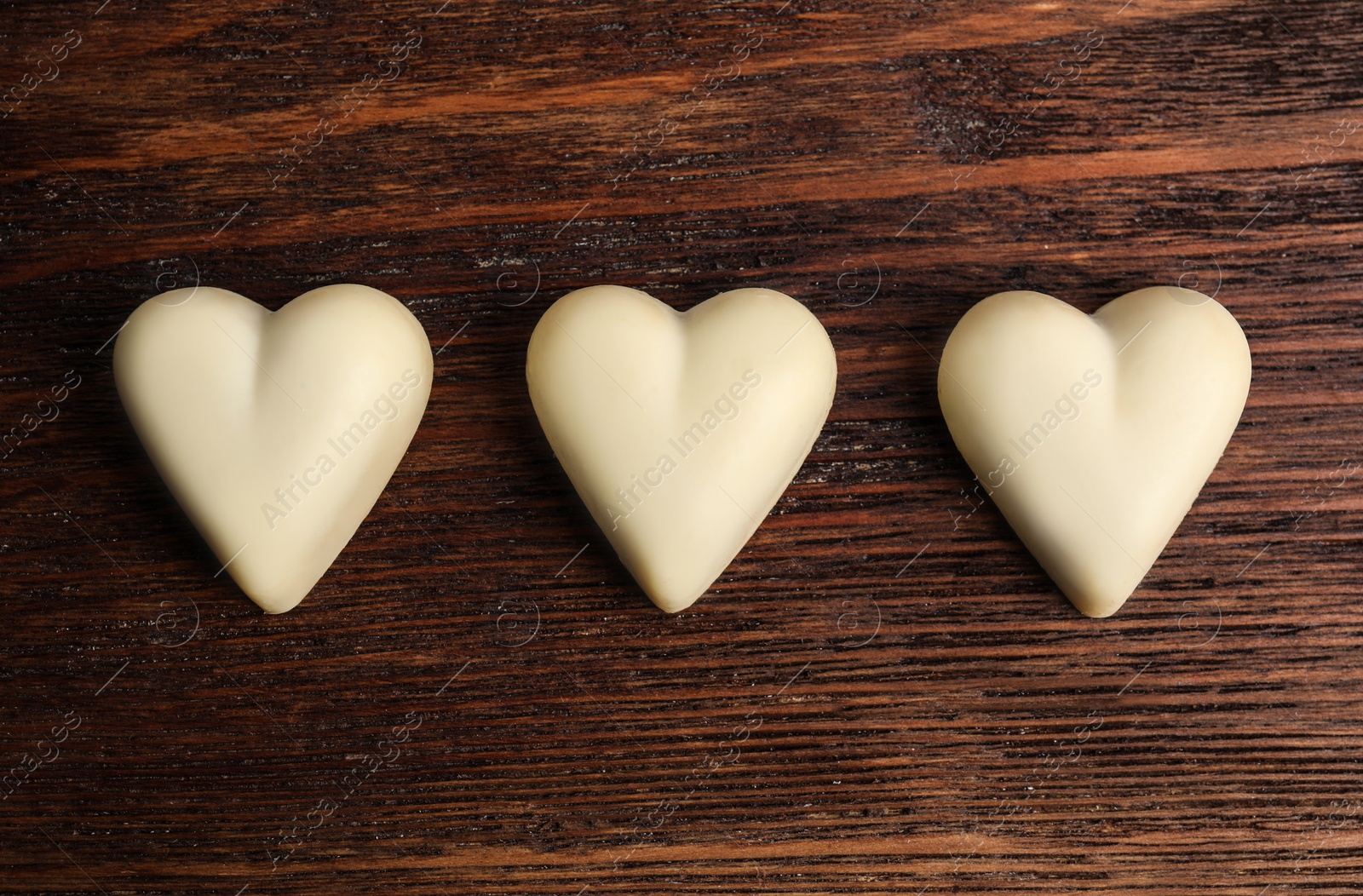 Photo of Tasty heart shaped chocolate candies on wooden table, flat lay. Happy Valentine's day