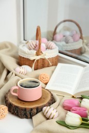 Photo of Easter decorations. Cup of coffee, painted eggs, tulips and book on windowsill