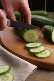 Photo of Woman cutting cucumber on wooden board at table, closeup