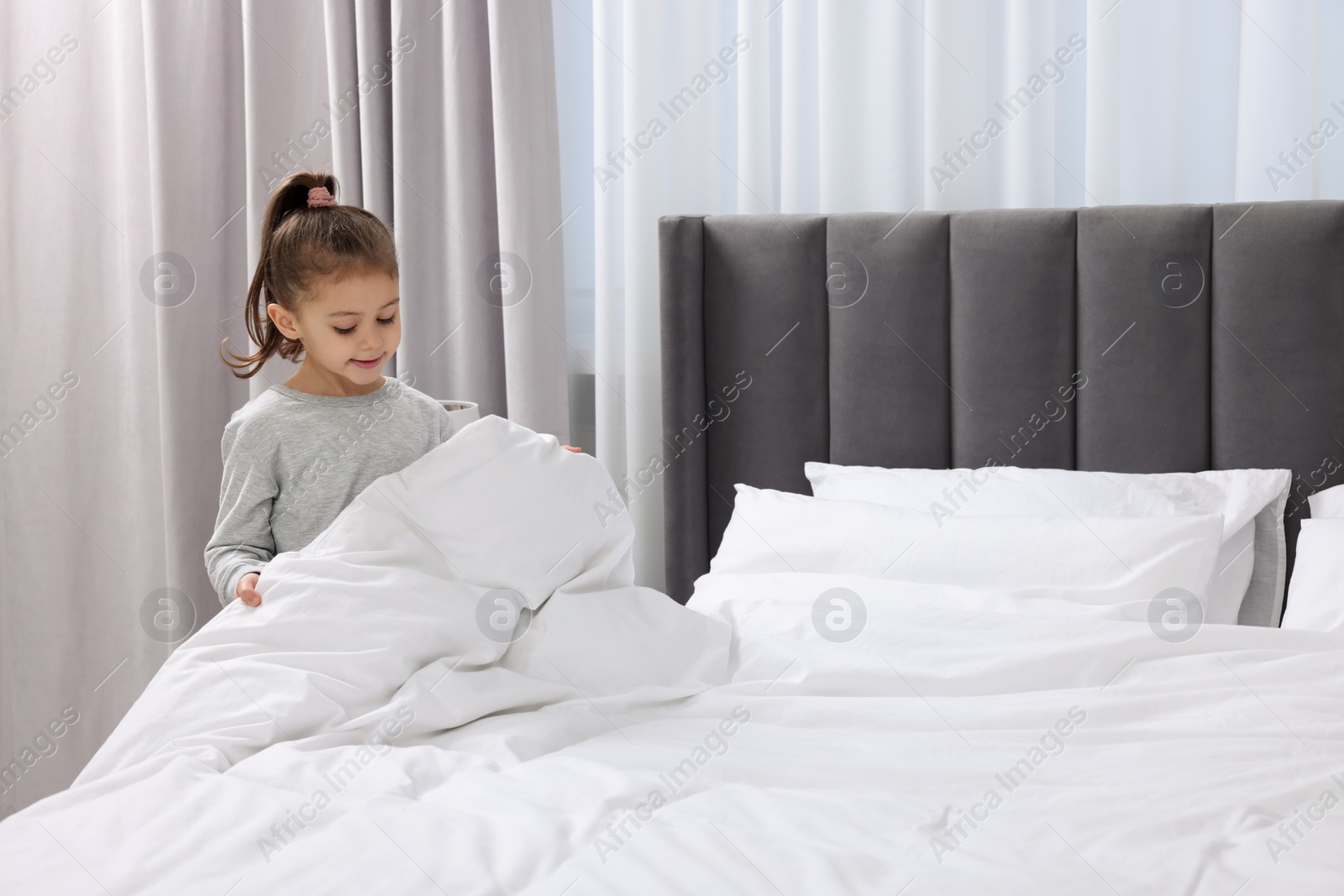 Photo of Cute girl changing bed linens in bedroom