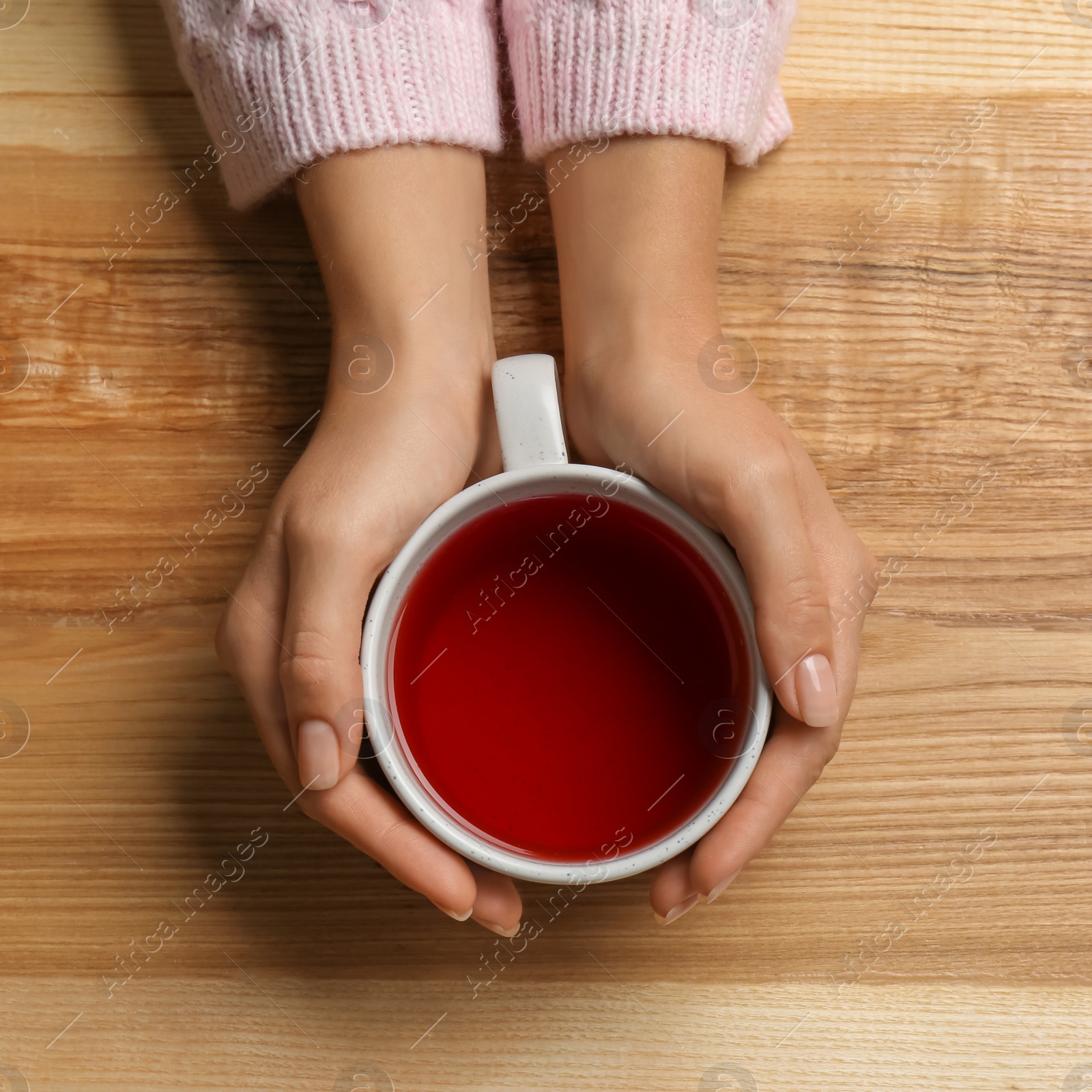 Photo of Woman holding cup of tea at wooden table, top view