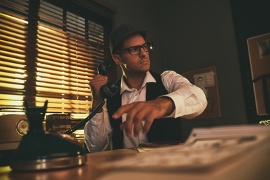 Photo of Old fashioned detective dialing telephone number at table in office