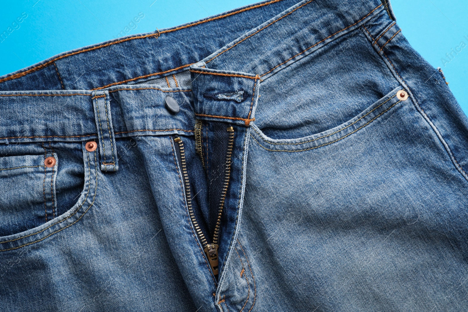 Photo of Jeans with unbuttoned fly on light blue background, top view. Exhibitionist concept