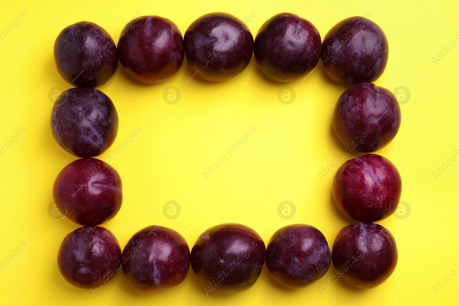 Photo of Frame made of delicious ripe plums on yellow background, flat lay. Space for text