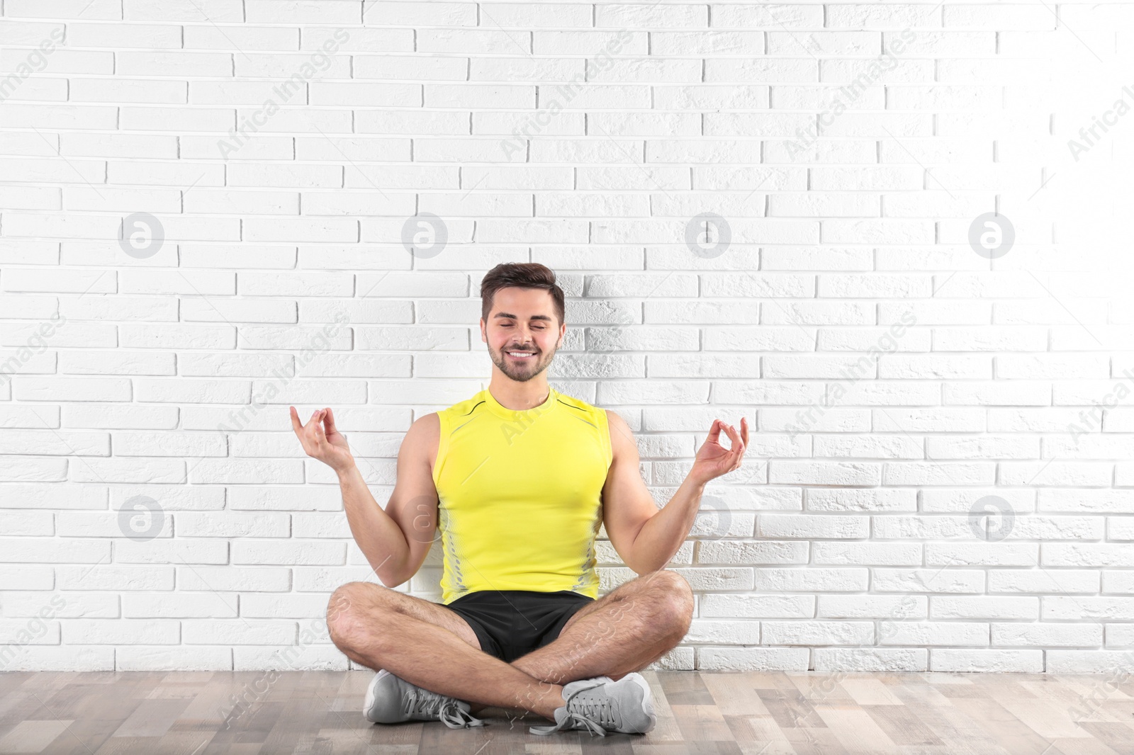 Photo of Handsome young man sitting on floor and practicing zen yoga near brick wall
