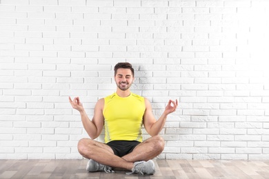 Handsome young man sitting on floor and practicing zen yoga near brick wall